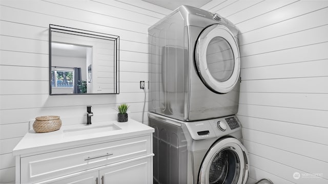 washroom with cabinets, stacked washer and dryer, wooden walls, and sink