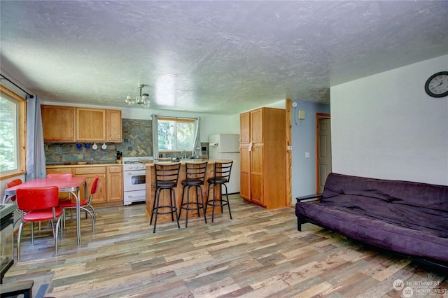 kitchen featuring tasteful backsplash, a textured ceiling, a kitchen breakfast bar, white appliances, and light hardwood / wood-style floors