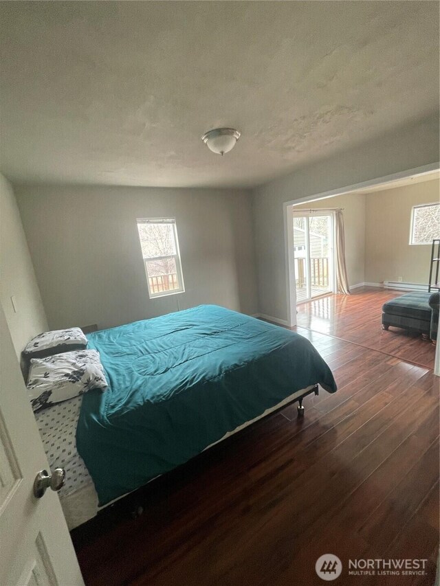 bedroom featuring multiple windows, a textured ceiling, baseboard heating, and wood finished floors