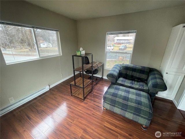 living area with a baseboard heating unit, dark wood-type flooring, baseboards, and a healthy amount of sunlight