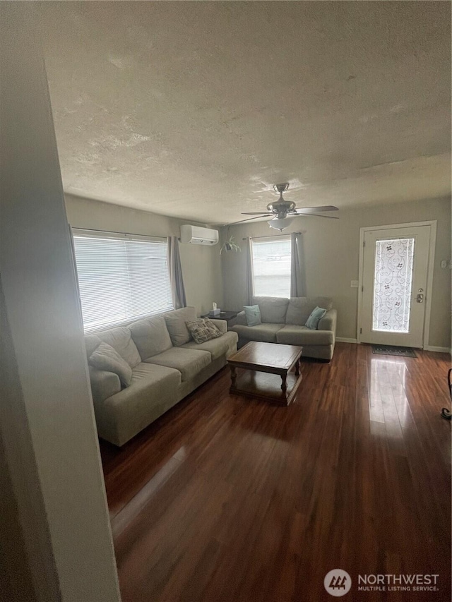 living room with dark wood-style floors, ceiling fan, a textured ceiling, a wall mounted air conditioner, and baseboards