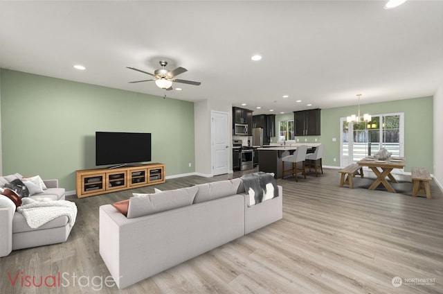 living room featuring sink, ceiling fan with notable chandelier, and light hardwood / wood-style floors