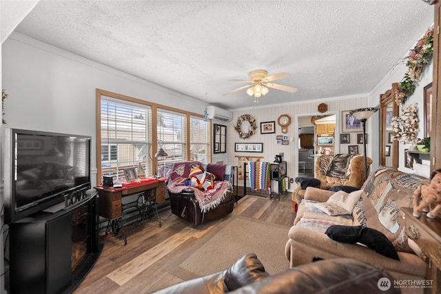 living area featuring a textured ceiling, ceiling fan, wood finished floors, an AC wall unit, and crown molding