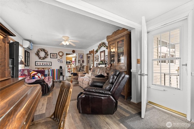 living area with a textured ceiling, wood finished floors, a ceiling fan, ornamental molding, and a wall mounted air conditioner