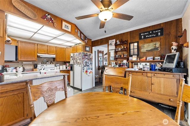 kitchen featuring a textured ceiling, under cabinet range hood, white appliances, wood walls, and a ceiling fan