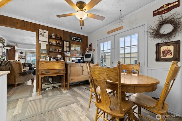 dining room with french doors, a wainscoted wall, ornamental molding, a textured ceiling, and light wood-type flooring