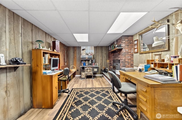 office with light wood-style floors, wooden walls, a drop ceiling, and built in study area