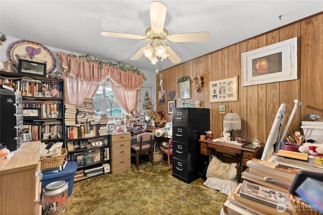 carpeted office with wooden walls and a ceiling fan