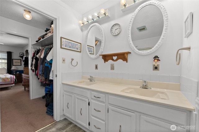 bathroom featuring a walk in closet, a sink, a textured ceiling, and double vanity