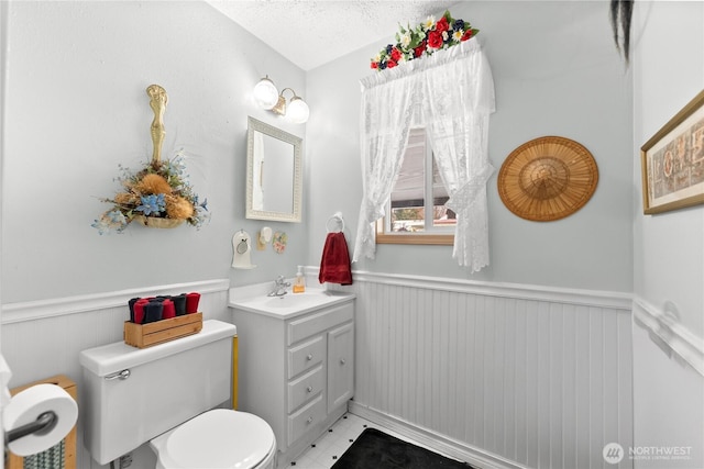 half bathroom featuring wainscoting, vanity, toilet, and a textured ceiling