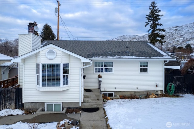 view of front facade featuring a chimney, fence, and roof with shingles