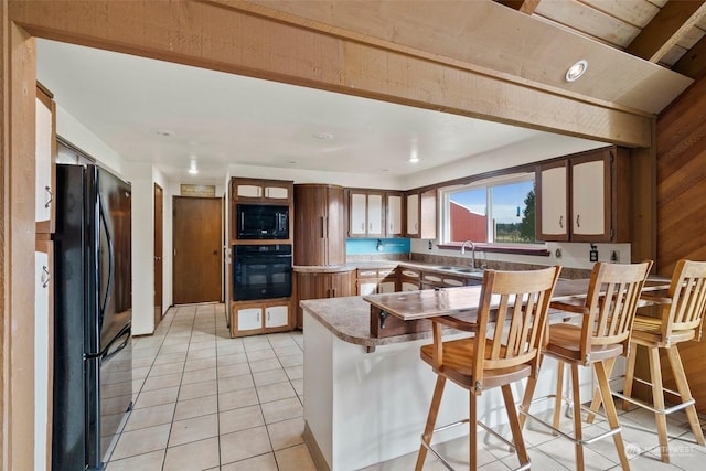 kitchen featuring light tile patterned flooring, a breakfast bar, sink, kitchen peninsula, and black appliances