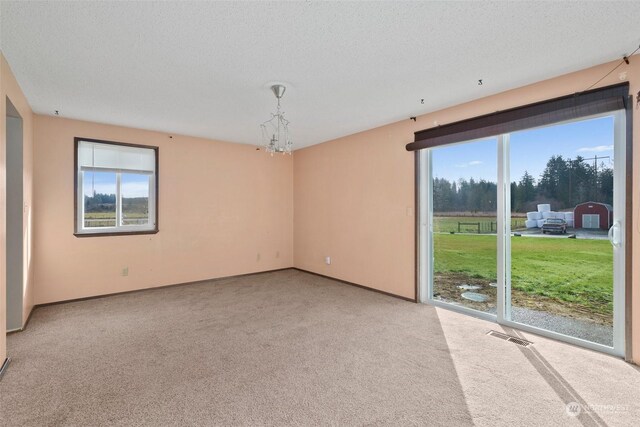 carpeted empty room featuring a chandelier, a textured ceiling, and a wealth of natural light