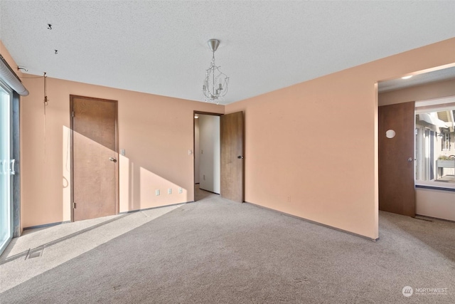 carpeted empty room featuring a wealth of natural light, a chandelier, and a textured ceiling