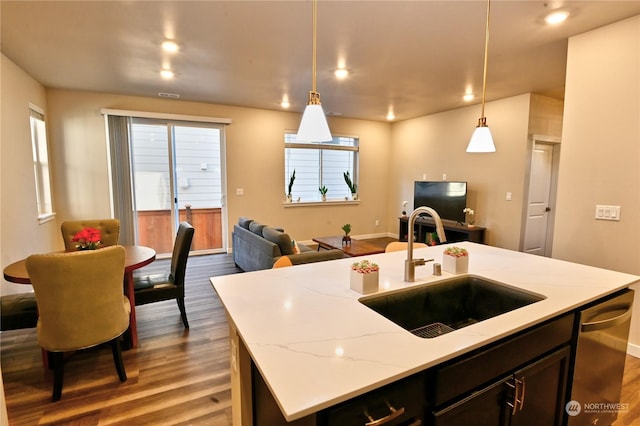 kitchen with sink, hardwood / wood-style flooring, hanging light fixtures, light stone counters, and a center island with sink