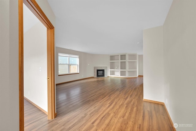 unfurnished living room featuring built in shelves and light wood-type flooring