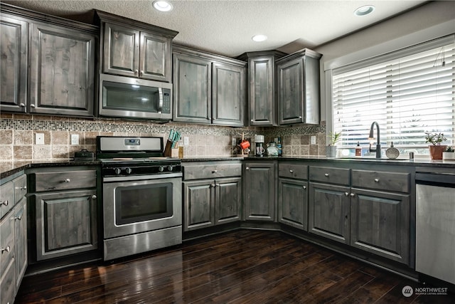 kitchen with sink, dark stone counters, dark hardwood / wood-style flooring, stainless steel appliances, and decorative backsplash