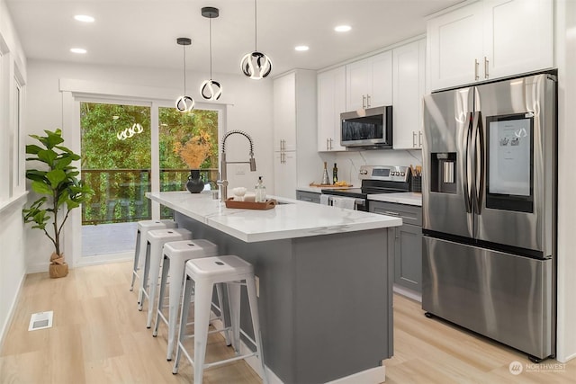 kitchen with sink, white cabinetry, decorative light fixtures, appliances with stainless steel finishes, and an island with sink