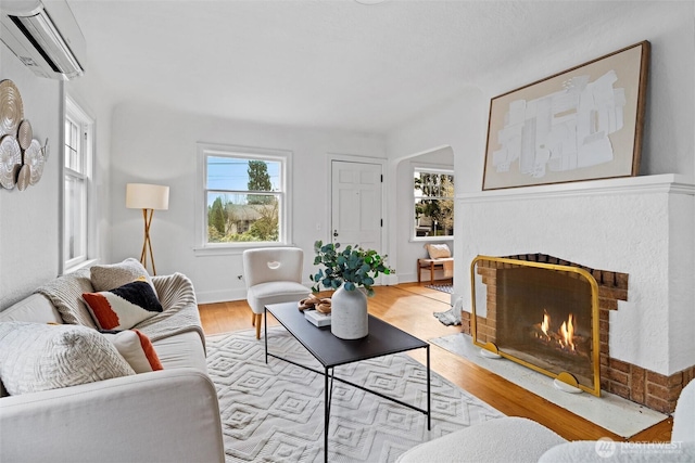 living room with baseboards, an AC wall unit, wood finished floors, and a warm lit fireplace