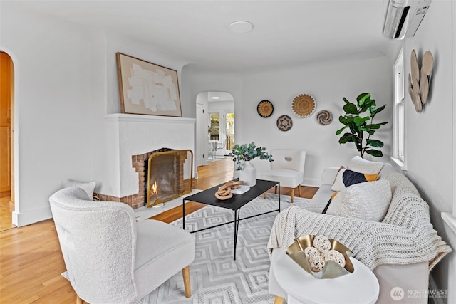 living area with wood finished floors, a fireplace, arched walkways, and a wall mounted AC