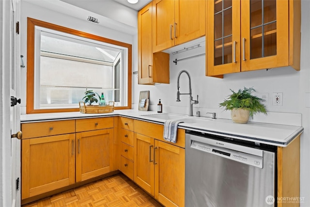 kitchen with a sink, glass insert cabinets, stainless steel dishwasher, and light countertops