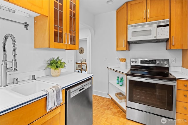 kitchen with glass insert cabinets, light countertops, brown cabinetry, stainless steel appliances, and a sink