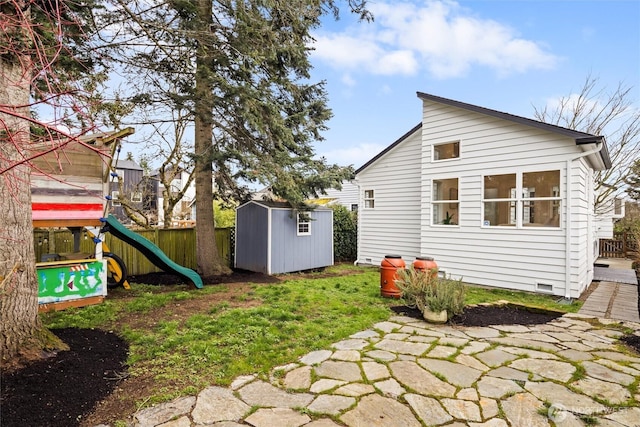 exterior space featuring a playground, fence, a shed, crawl space, and an outbuilding