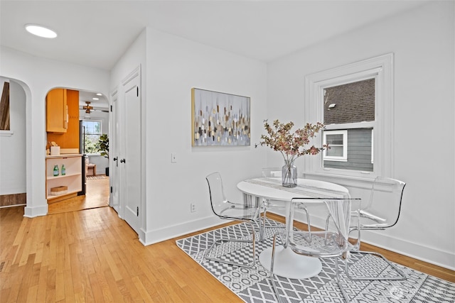 dining space featuring baseboards, arched walkways, and light wood finished floors