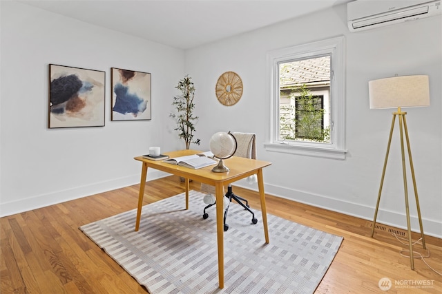 office featuring light wood-style floors, baseboards, and a wall mounted air conditioner