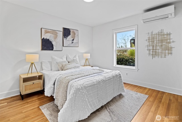 bedroom with light wood finished floors, baseboards, and a wall unit AC