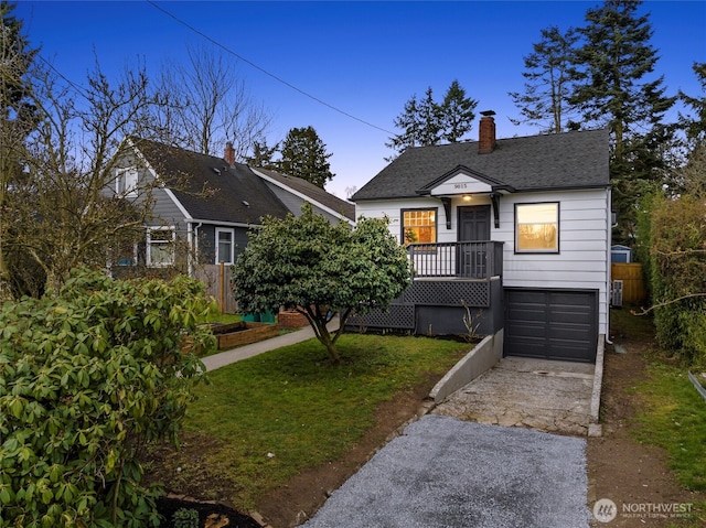 view of front of house with an attached garage, a shingled roof, a chimney, concrete driveway, and a lawn