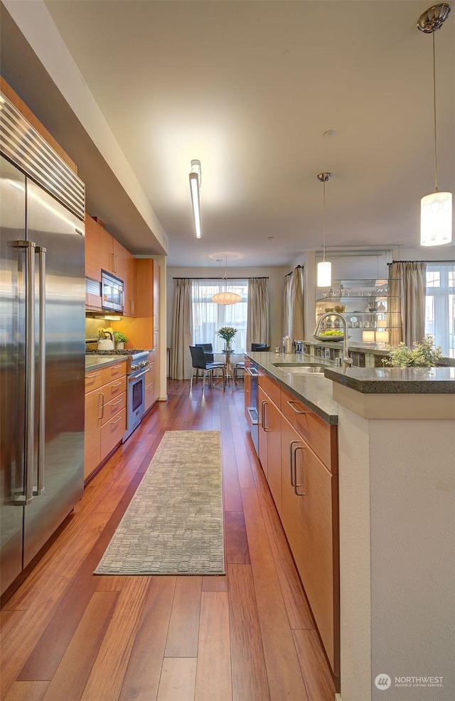 kitchen with pendant lighting, high quality appliances, sink, and hardwood / wood-style floors