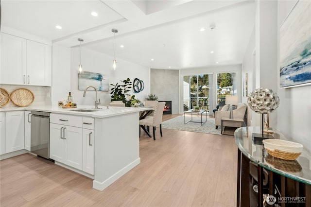 kitchen featuring sink, light wood-type flooring, dishwasher, a fireplace, and white cabinets