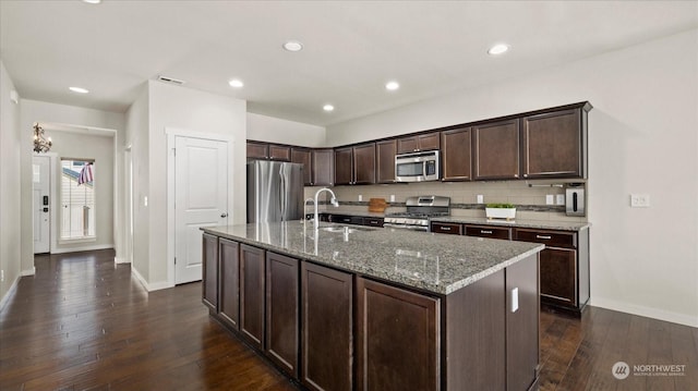 kitchen with sink, stainless steel appliances, light stone countertops, and a center island with sink