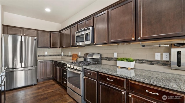 kitchen featuring stainless steel appliances, light stone countertops, dark wood-type flooring, and dark brown cabinetry