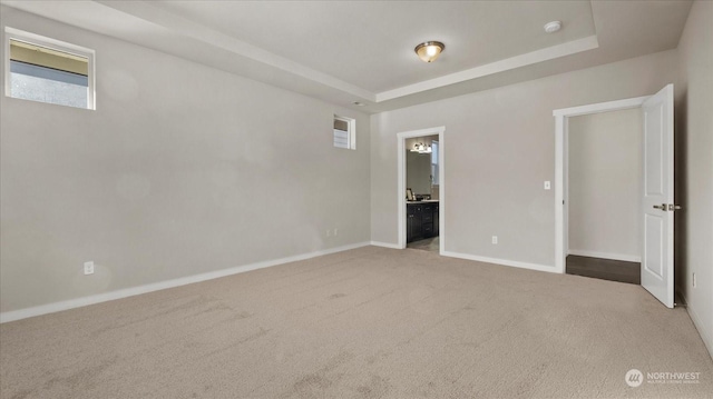 unfurnished bedroom featuring connected bathroom, a raised ceiling, and light carpet