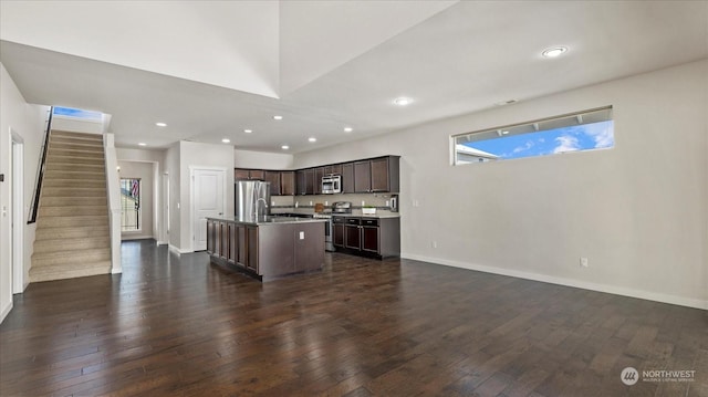 kitchen featuring appliances with stainless steel finishes, a kitchen island with sink, dark wood-type flooring, plenty of natural light, and dark brown cabinets