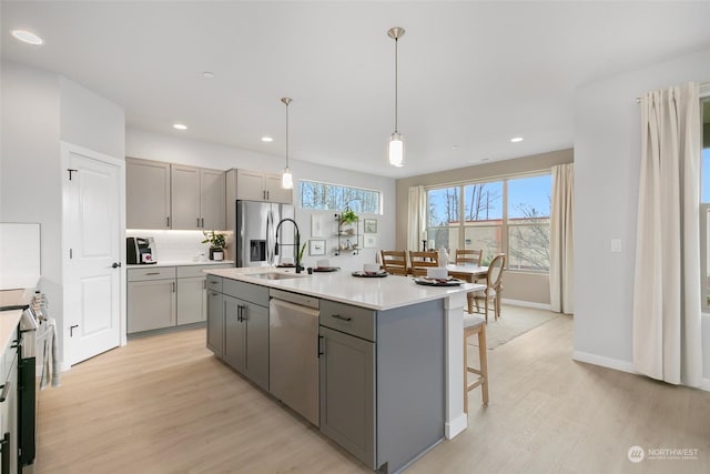 kitchen with appliances with stainless steel finishes, pendant lighting, gray cabinetry, a kitchen island with sink, and light wood-type flooring