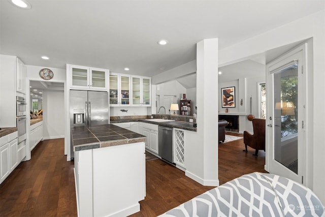 kitchen with dark wood-type flooring, sink, appliances with stainless steel finishes, kitchen peninsula, and white cabinets