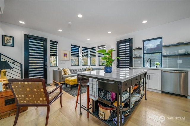 kitchen with stainless steel dishwasher, a kitchen island, light hardwood / wood-style flooring, and white cabinets