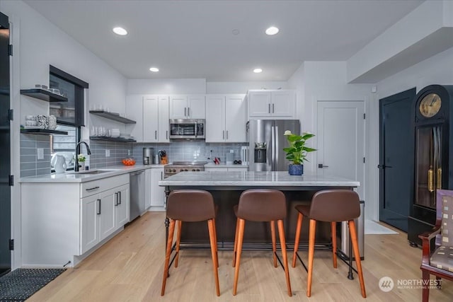 kitchen featuring a breakfast bar area, appliances with stainless steel finishes, white cabinetry, a kitchen island, and light wood-type flooring