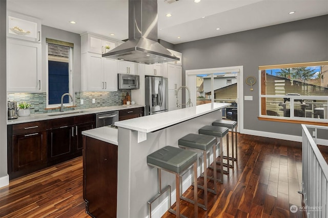 kitchen with sink, appliances with stainless steel finishes, a kitchen breakfast bar, island range hood, and a center island with sink