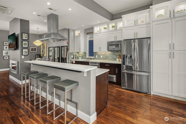 kitchen with appliances with stainless steel finishes, island range hood, white cabinets, a kitchen bar, and a center island with sink