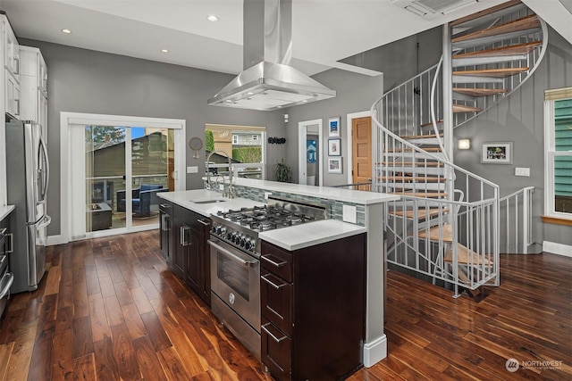 kitchen featuring appliances with stainless steel finishes, island exhaust hood, dark wood-type flooring, dark brown cabinets, and a center island with sink