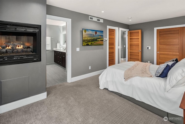 bedroom with a multi sided fireplace, light colored carpet, and ensuite bathroom