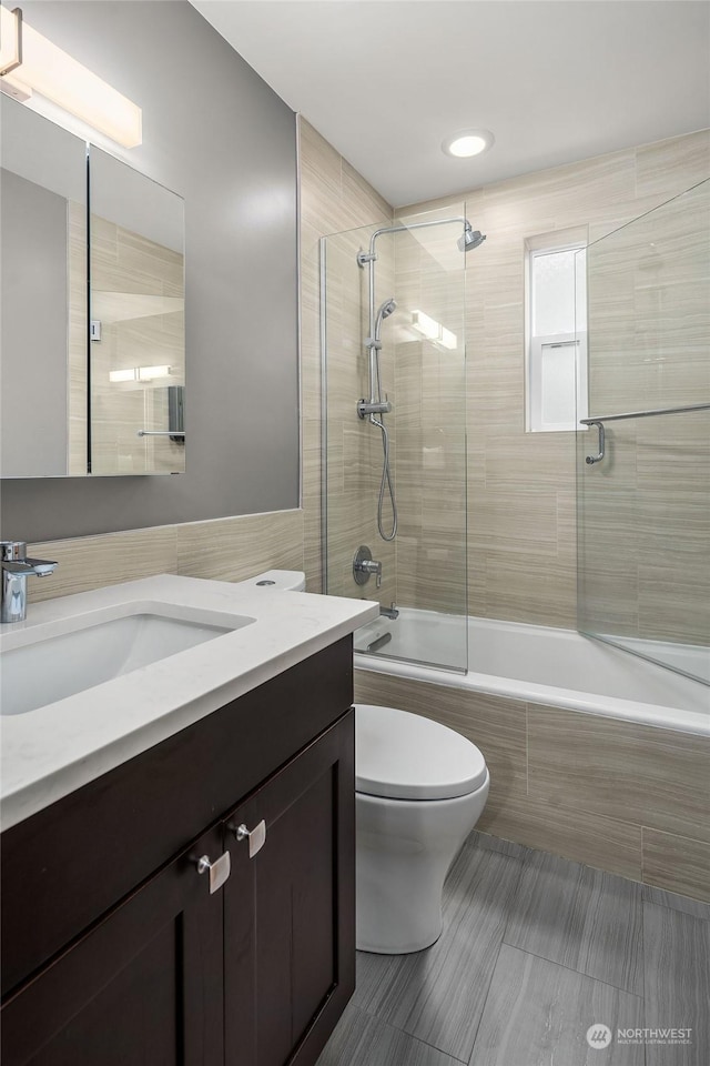 full bathroom featuring shower / bath combination with glass door, tile walls, vanity, tile patterned floors, and toilet