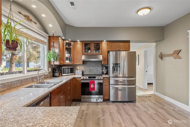 kitchen featuring sink, light stone counters, light wood-type flooring, stainless steel appliances, and backsplash