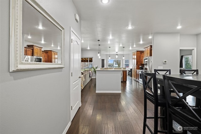 kitchen with a breakfast bar area, appliances with stainless steel finishes, a center island, dark hardwood / wood-style flooring, and decorative light fixtures