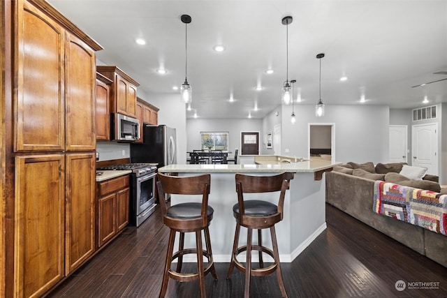 kitchen featuring a kitchen bar, appliances with stainless steel finishes, dark hardwood / wood-style floors, an island with sink, and pendant lighting