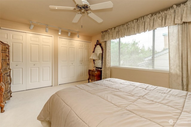 bedroom with light carpet, two closets, and ceiling fan